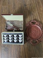 Photo showing the steak knife set in box with wooden handles and the carved solid wood teacup tray with floral patterns and handles on a wood floor.