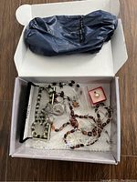 Top-down view of box containing assorted necklaces, ring in red box, and pouch.