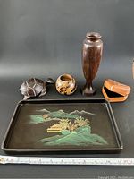 Photo showing the assorted wooden items on black background including the lacquered tray with painted landscape, wooden vase, bowl, turtle figurine, and box.