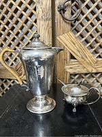 Photo of the full two-piece Birks silverware set featuring the tall pot with woven handle and the small sugar bowl with lid and spoon on a black surface.