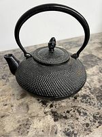 Black cast iron antique teapot with hobnail texture, curved spout, and handle on stone surface