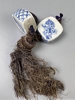 Close-up of two porcelain painting weights connected by a braided cord with a worn tassel, showing traditional blue designs on white porcelain.