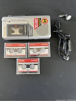 Full view of AIWA microcassette recorder with 3 Sony microcassette tapes and earphones on black surface.