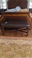 Front view of the wood and leather-like upholstered bench placed in front of a wooden bedframe on a patterned rug.