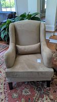 Front view of beige suede-like fabric armchair with matching throw pillow on a patterned rug.