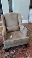 Full front view of beige Pottery Barn armchair with throw pillow on the seat, located on a patterned rug with wooden floor visible.