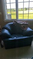 Front view of the black leather chair with the multicolored throw blanket draped on top near a window.