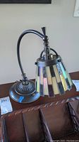 Full view of the desk lamp showing the curved metal arm, round base, and stained glass shade with shades of white and iridescent colors.