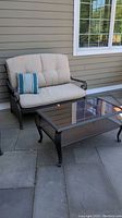 Full view of loveseat with cushions and matching glass top coffee table on patio.