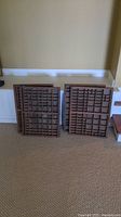 Four wooden printing press trays arranged standing against a wall on carpeted floor, showing front with multiple compartments.