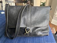 Black leather Ralph Lauren messenger bag shown on table, displaying front flap, strap, and buckle details.