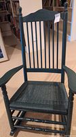 Full front view of black wooden rocking chair with vertical slat back and turned arms.