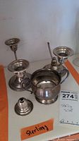 Photo showing two sterling silver candlesticks and one sugar bowl with a MaxSold tag and a label 'Sterling', one candlestick's top is broken.