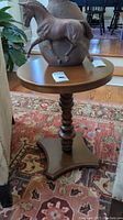 Side angle view of the round wooden side table with a horse statue on top, showing the tabletop surface and part of the pedestal.