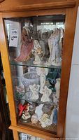 Three-shelf cabinet view with multiple angel figurines and glass pieces