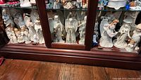 Wide shot showing multiple angel figurines of various sizes, styles, and materials displayed in a cabinet.