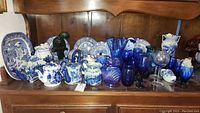 Wide view of Liberty Blue ceramic dishes, serving pieces and blue glassware arranged on wood shelf