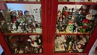Full view of the middle shelf cabinet with the Christmas collectibles arranged inside behind glass doors showing various Santa, snowmen, and other holiday figurines.