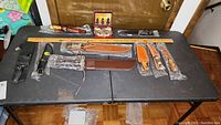 Overview of commemorative and decorative knives of various styles, sheaths, and packaging displayed on black folding table.