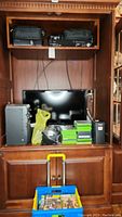 Wooden hutch opening showing two black carrying cases on top shelf and television with electronics below.