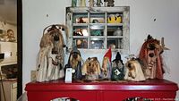 Seven gnome figurines arranged on red surface beneath hanging shelf