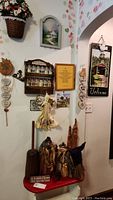 Photo of corner display with the gnomes on the red and white bench, surrounded by hanging wall décor including plaques, fabric accessories, and a small spice rack shelf.