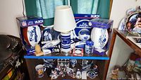 Wide view of multiple Penn State collectibles including lamp, ball sets, footballs, jars, and teddy bear on display shelf.