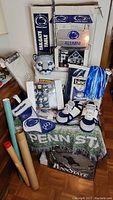 Overview showing the full set of Penn State collectible items including blanket, slippers, mascot head, pom-pom, audio cooler, and boxed tailgate table.