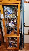 Tall wooden and glass display cabinet containing Penn State memorabilia including decor plates, model cars, figurines, and mugs.