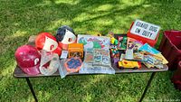 Full lot laid out on table showing sports helmets, collectible cards, Rubik's cube, toy car, books, and metal sign.