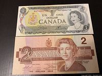 Front side of one and two dollar Canadian bills, showing portraits of Queen Elizabeth II and Bill details.