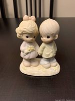 Ivory porcelain figurine of a boy and girl holding hands, girl holding flowers, standing on floral base.