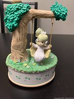 Front view of Enesco Precious Moments musical figurine showing girl on swing hanging from tree base with 'I love you' carved heart detail.