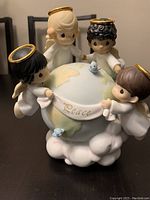 Front view of four angels holding globe with word 'Peace' and blue birds sitting on it.