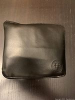 Black faux leather zippered pouch with embossed HT logo on front, fully zipped closed.