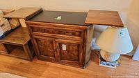 Full front view of the wooden buffet board with side panels extended, showing the base cabinet with doors and drawer, black center top, and two wooden side wings.