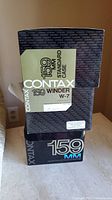 Boxes for Contax 159 standard case and W-7 winder stacked on table, showing front of boxes with branding and model numbers.