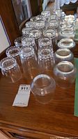 Overall view of multiple crystal tumblers and hi-ball glasses arranged on a wooden surface.
