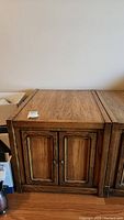 Photo showing the front and top of one wooden end table with two paneled doors and metal knobs.
