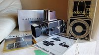 Front three-quarter view of camera body with lens and hood, waist level finder, original box, manuals and reference book.