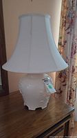 Full view of white ceramic tri-light lamp with stained fabric shade on wooden surface.