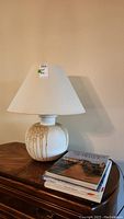 Full view of shaded table lamp with four hardcover books stacked beside it on wooden furniture.