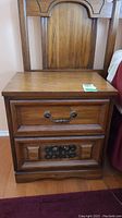 Front view of the vintage wood night table showing two drawers with metal handles and carved details, scratches and one missing handle visible.