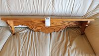 Full view of wooden wall shelf with carved detailing, resting on a light-colored leather couch.