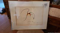 Full view of framed print showing stylized bird artwork with light wood floor and furniture in background.