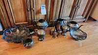 Full view of the silver plated tea set and serving baskets with all pieces arranged on wooden floor.