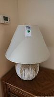 Full view of the lamp with shade in natural light, showing overall shape and texture of ceramic base.