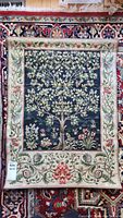 Full view of tapestry showing the entire rectangular design with a floral tree and ornate border, placed on a patterned rug.