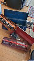 Two vintage metal toolboxes, blue and red, with their trays and vintage tools inside, placed on wooden floor
