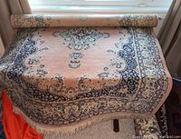 Rolled and partially unrolled view of pink floral medallion patterned area rug with fringe edges